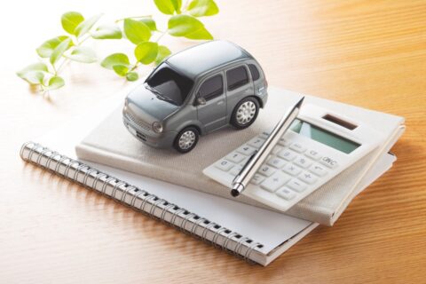 A small grey car on top of a calculator and a pen.