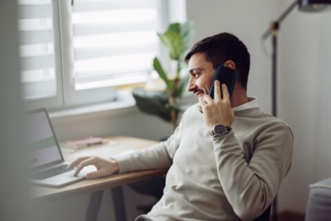 A young man talking on his smartphone while using a laptop